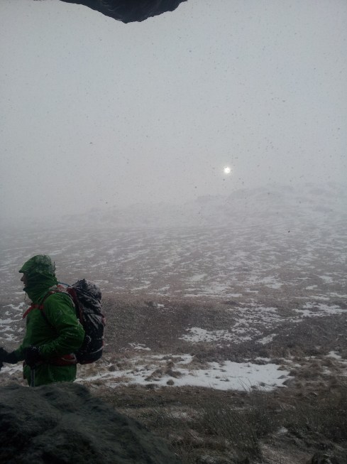 view from under the rock.  Foolhardy codger hikes past sun shrouded in yet more snow.